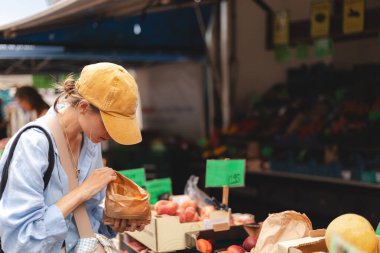 Kadın müşteri manavda günlük kıyafetlerini giyer ve taze organik sebzeleri seçer. Framer 's Market' ten taze ham ürün ve bakkaliye alan genç bir kadının portresi.