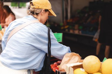 Kadın müşteri manavda günlük kıyafetlerini giyer ve taze organik sebzeleri seçer. Framer 's Market' ten taze ham ürün ve bakkaliye alan genç bir kadının arkası..