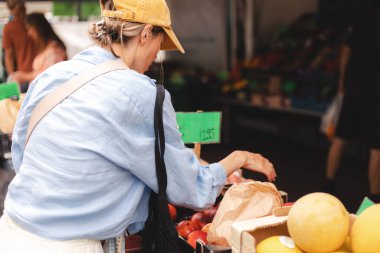 Kadın müşteri manavda günlük kıyafetlerini giyer ve taze organik sebzeleri seçer. Framer 's Market' ten taze ham ürün ve bakkaliye alan genç bir kadının arkası..