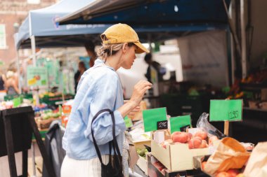 Kadın müşteri manavda günlük kıyafetlerini giyer ve taze organik sebzeleri seçer. Framer 's Market' ten taze ham ürün ve bakkaliye alan genç bir kadının portresi.
