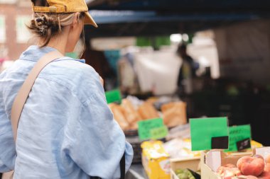 Kadın müşteri manavda günlük kıyafetlerini giyer ve taze organik sebzeleri seçer. Framer 's Market' ten taze ham ürün ve bakkaliye alan genç bir kadının arkası..