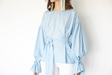 Kabarık kollu ve kemerli mavi elbiseli bir kadının fotoğrafı. Kadın kıyafetlerinin ayrıntıları. Zarif gömlek giyen ve beyaz arka planda uzun boncuklu küpeler takan bir kadının moda detaylarını kapat..