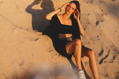 Siyah tişörtlü, kısa saçlı, genç, güzel esmer kadın gün batımında kumların üzerinde oturuyor. Kız rahat ve mutludur. Düşünceli kız dinleniyor, saçını düzeltiyor..