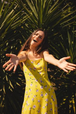 Uzun saçlı, mutlu bir kadın, palmiye ağacının yanında çiçek desenli sarı bir elbise giyer, kucaklaşmak için ellerini açar, sarılmak için bana gelir. Turist kız tanıştığımıza memnun oldum! Hoş geldiniz.!