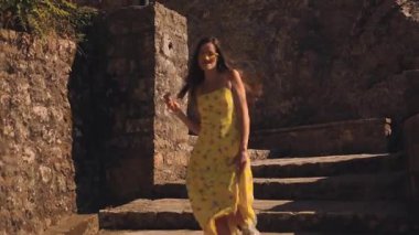 Seçici odaklanma, eski kasaba. Turist esmer, uzun saçlı, uzun sarı elbiseli, güneş gözlüklü, yürüyen dans eden, merdivenlerde şarkı söyleyen, dondurma yiyen, yaz sıcağında arkasını dönen, saçını düzelten bir kadın.. 