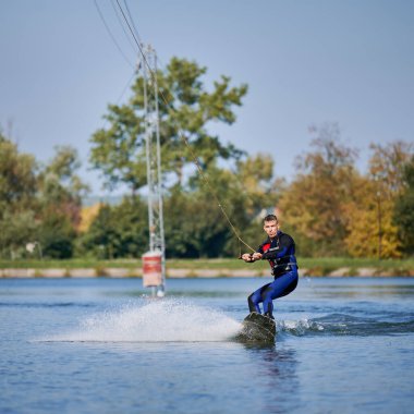 Wakeboardcu gölde sörf yapıyor. Genç sörfçü kablo parkında sörf yaparken eğleniyor. Su sporu, açık hava aktivitesi konsepti.