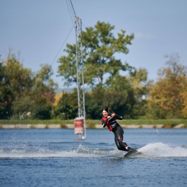 Wakeboardcu gölde sörf yapıyor. Genç sörfçü kablo parkında sörf yaparken eğleniyor. Su sporu, açık hava aktivitesi konsepti.