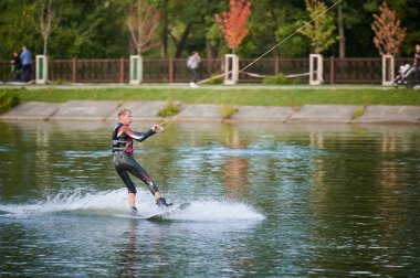 Wakeboardcu gölde sörf yapıyor. Genç sörfçü kablo parkında sörf yaparken eğleniyor. Su sporu, açık hava aktivitesi konsepti.