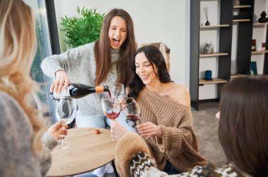 Young women enjoying winter weekends inside contemporary barn house. Four girls having fun and drinking wine.