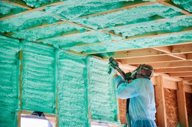 Male builder insulating wooden frame house. Man worker spraying polyurethane foam inside of future cottage, using plural component gun. Construction and insulation concept. clipart