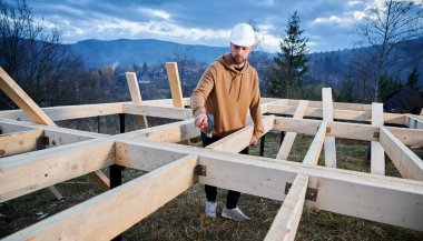 Erkek işçiler temel üzerine ahşap çerçeve inşa ediyorlar. Marangozlar kereste iskeleti için ahşap kiriş döşüyorlar, çekiç kullanıyorlar. Marangozluk kavramı.