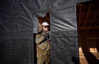 Erkek müteahhit gelecekteki kulübenin duvarına su geçirmez zar takıyor. Ahşap çerçeve inşa eden bir işçi. Marangozluk ve inşaat konsepti.