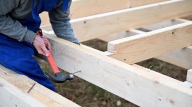 Man worker building wooden frame house. Carpenter hammering nail into wooden truss, using hammer. Carpentry concept.