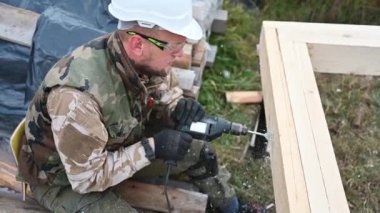 Ahşap çerçeve inşa eden adam. Gelecekteki kulübelerin ahşap çerçevesinde elektrikli matkapla delik açan işçiler. Marangozluk kavramı.