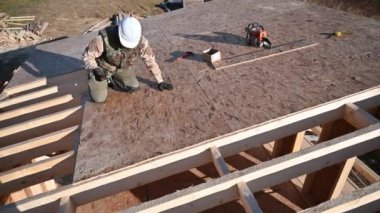 Marangoz, gelecekteki kulübenin çatısında OSB paneline çivi çakıyor. Ahşap çerçeve inşa eden bir işçi. Marangozluk ve inşaat konsepti.
