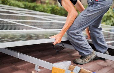 Man technician mounting photovoltaic solar moduls on roof of house. Cropped view of electrician installing solar panel system outdoors. Concept of alternative and renewable energy. clipart