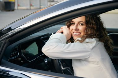 Siyah arabada poz veren neşeli kadın girişimcinin portresi dümenciliğin ve iş yerine gitmenin tadını çıkarıyor, başarılı beyaz işveren şirket otomobilinde kameraya gülümsüyor.