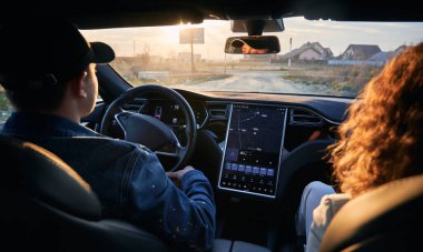 Arabanın içinde dikiz aynası var. Sürücü ve yolcu toprak yolda dokunmatik ekranla modern kullanıcı arayüzü ile elektrikli araba ile seyahat ediyorlar. Erkek şoför seyrüsefer sistemini kullanarak araziye çıkıyor..