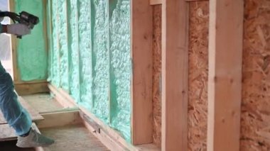 Erkek müteahhit ahşap iskeleti yalıtıyor. Adam işçi, gelecekteki kulübenin içine poliüretan köpük püskürtüyor, çoğul bileşen silah kullanıyor. İnşaat ve yalıtım konsepti.