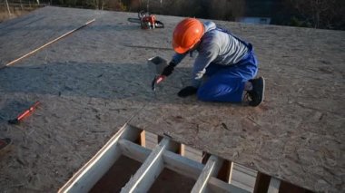Marangoz, gelecekteki kulübenin çatısında OSB paneline çivi çakıyor. Ahşap çerçeve inşa eden bir işçi. Marangozluk ve inşaat konsepti.