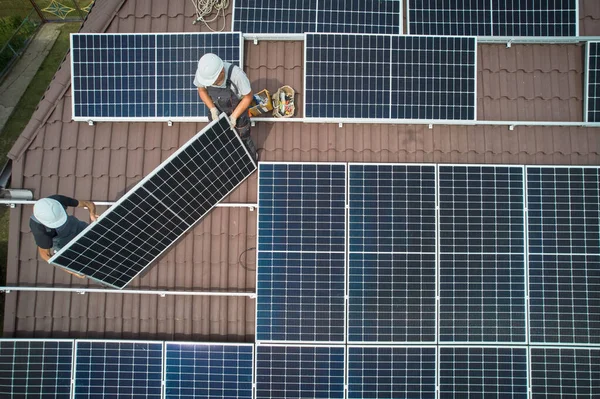 屋根の上に太陽光発電モジュールを設置する男性労働者 屋外で太陽電池パネルシステムを構築するヘルメットのエンジニア 代替エネルギーと再生可能エネルギーの概念 空中風景 — ストック写真