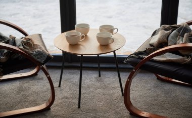 Küçük masada dört fincan bitmemiş çay ve kafede kareli ekose koltuklar dizayn edilmiş. Gündüz vakti pencerenin önünde sandalyeleri olan tahta masanın üzerindeki beyaz bardakların önü. Dinlenme kavramı.