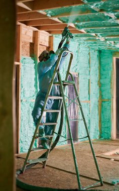 Erkek müteahhit ahşap iskeleti yalıtıyor. Adam işçi, gelecekteki kulübenin içine poliüretan köpük püskürtüyor, merdiven üzerinde duruyor, çoğul bileşen silah kullanıyor. İnşaat ve yalıtım konsepti.