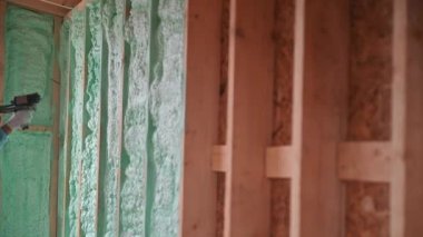 Erkek müteahhit ahşap iskeleti yalıtıyor. Adam işçi, gelecekteki kulübenin içine poliüretan köpük püskürtüyor, çoğul bileşen silah kullanıyor. İnşaat ve yalıtım konsepti.