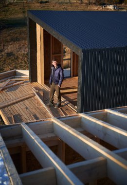 Erkek mühendis ahşap çerçeve inşa ediyor. İnşaat alanında terasta duran bir adam, akşamları iş kalitesini kontrol ediyor..