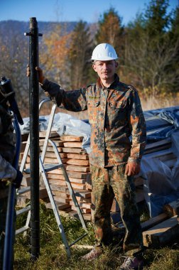 Erkek işçi ahşap çerçeve için temel inşa ediyor. Güneşli bir günde beyaz kasklı bir insan müteahhitinin portresi yere kazık çakıyor..