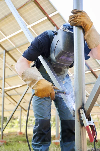 Kaynak makinesi ile kaynak yapan kaynak makinesi güneş panelleri için. Yenilenebilir ve ekolojik enerji kavramı. Çevre fikri güvenli. Koruyucu kask takan işçi iş kıyafeti giyiyor.