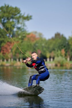 Wakeboardcu gölde sörf yapıyor. Genç sörfçü kablo parkında sörf yaparken eğleniyor. Su sporu, açık hava aktivitesi konsepti.