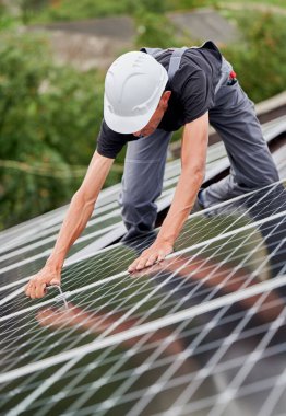 Man technician mounting photovoltaic solar moduls on roof of house. Electrician in helmet installing solar panel system outdoors, tightening with hex key. Concept of alternative and renewable energy.