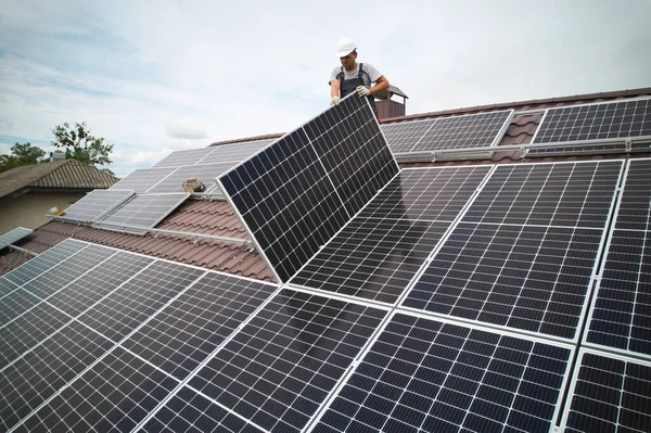 Man technician mounting photovoltaic solar moduls on roof of house. Mounter in helmet installing solar panel system outdoors. Concept of alternative and renewable energy. Aerial view.