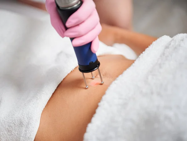 Female client receiving laser treatment in cosmetology clinic. Close up doctor cosmetologist using erbium ablative laser machine while performing lifting procedure on woman abdomen.