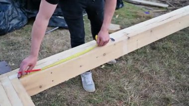 Man worker building wooden frame house on pile foundation. Close up carpenter using tape measure for measuring wooden planks and making marks. Carpentry concept.