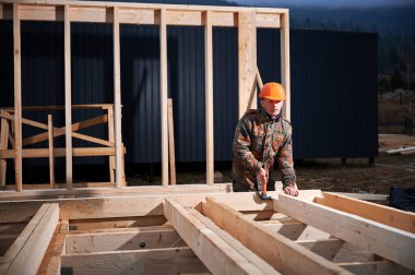 Yığınla temele ahşap çerçeve inşa eden bir işçi. Marangoz çekiçle tahta çiviyi çekiçle çakıyor. Marangozluk kavramı.