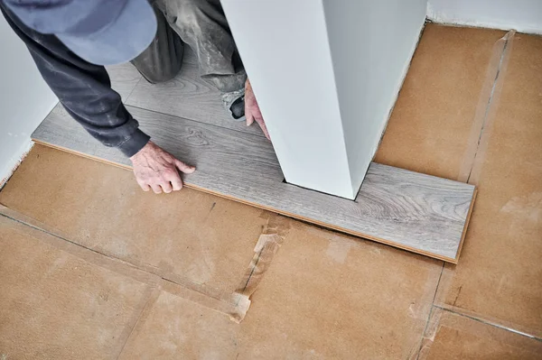 Close up of male hands laying laminate planks on the floor in flat under renovation. Man construction worker installing timber laminate flooring at home. Hardwood floor renovation concept.