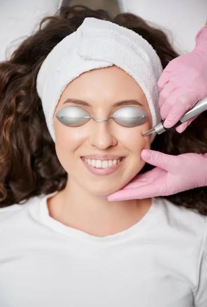 Close up of young girls face on cosmetic skin care procedure. Cropped view of hands of beautician, who locally and painlessly removing visible dilated vessels of face, using modern laser energy.