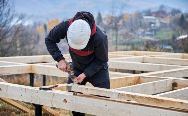 Yığınla temele ahşap çerçeve inşa eden bir işçi. Marangoz çekiç ve tornavida kullanarak ahşap tahtalar için mobilya kuruyor. Marangozluk kavramı.