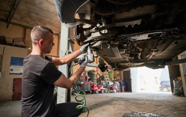 Mechanic, engineer servicing car in garage, auto center. Hardworking, strong man holding equipment by hands, drilling, looking. Concept of repairing, fixing car.