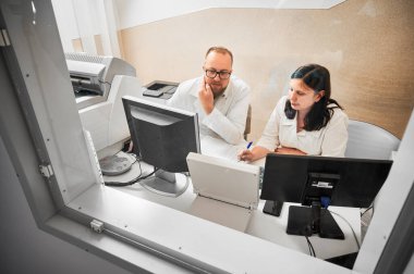 Medical computed tomography or MRI scanner. Side view of two specialists sitting at computer, working in hospital. Doctors looking at MRI results. Concept of medicine and healthcare.