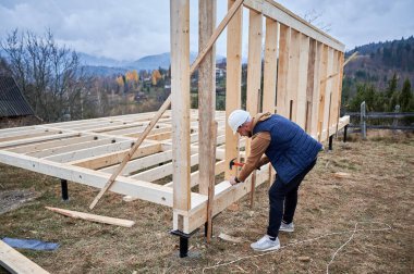 Yığınla temele ahşap çerçeve inşa eden bir işçi. Marangoz çekiçle tahta çivi çakıyor. Marangozluk kavramı.