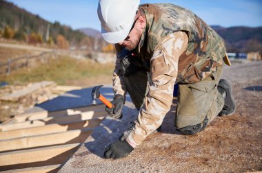 Marangoz, gelecekteki kulübenin çatısında OSB paneline çivi çakıyor. Ahşap çerçeve inşa eden bir işçi. Marangozluk ve inşaat konsepti.