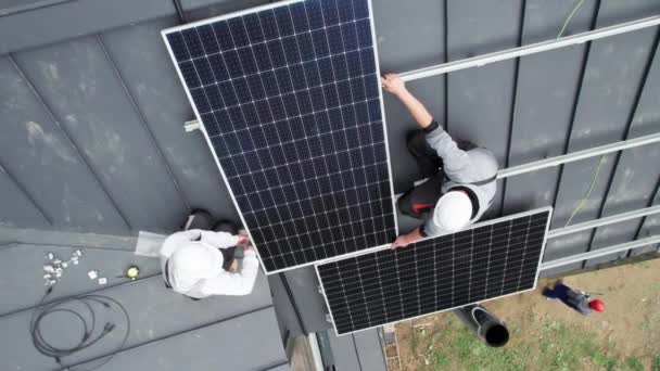 屋根の上に太陽光発電パネルを設置する技術者の空中トップビュー ヘルメットの男性エンジニアは 16進キーの助けを借りて太陽電池モジュールシステムを構築します 再生可能エネルギーの概念 — ストック動画
