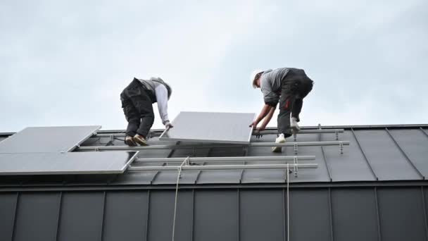 技术人员在房顶上安装太阳能电池板系统 戴钢盔的男工在室外携带光电太阳能组件 替代能源和可再生能源的概念 — 图库视频影像