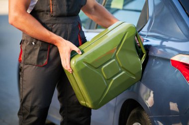 Profesyonel işçinin benzinle doldurduğu bozuk bir araba. Delikanlı benzin deposunu teneke kutudan dolduruyor. Mavi arabayı dolduran işçi önlüklü adam manzarası..