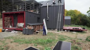 Teknisyen evin çatısına güneş paneli kuruyor. Dışarıda fotovoltaik güneş modülü taşıyan kasklı bir işçi. Alternatif ve yenilenebilir enerji kavramı.