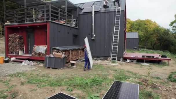 在房顶上安装太阳能电池板系统的技术员 头戴头盔的男工在室外携带光电太阳能组件 替代能源和可再生能源的概念 — 图库视频影像