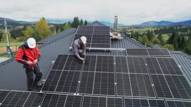 Teknisyenler evin çatısına fotovoltaik güneş panelleri kuruyor. Miğferli erkek mühendislerin güneş modülü sistemi inşa etmelerini gösteren insansız hava aracı görüntüsü. Alternatif, yenilenebilir enerji kavramı.